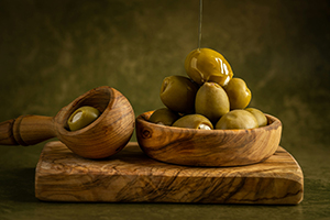 A wooden bowl of olives with golden olive oil
